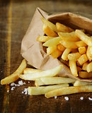 Traditional potatoes French fries with salt on wooden background