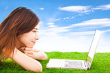 pretty young woman lying on a meadow with laptop