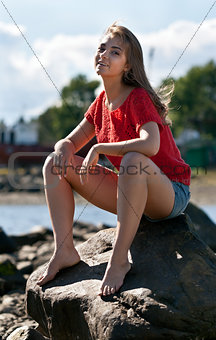 girl in a red sweater sits on a rock