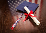 Graduation Cap and Diploma on Table with American Flag Reflection