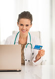 Portrait of happy medical doctor woman with credit card and lapt