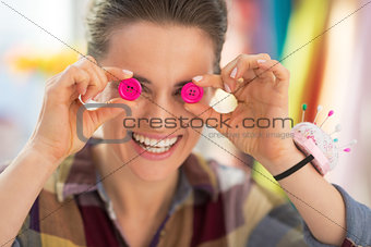 Happy seamstress holding buttons in front of eyes