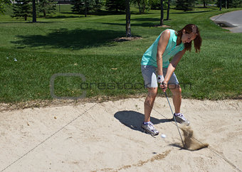Woman swings at the golf ball caught in the sand trap
