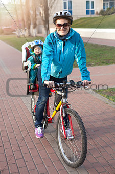 Caucasian young woman on a bicycle with little son behind