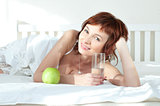 attractive young woman with an green apple and glass of water at bed
