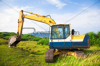 excavator on the meadow with sky and ocean background