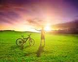 backpacker standing next to bicycle with sunset background