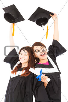 two happy young graduate students holding hats and diploma