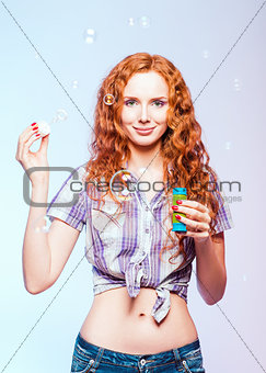 Beautiful smiling redhead girl blows bubbles. Studio portrait 