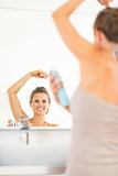 Happy young woman applying deodorant on underarm in bathroom