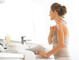 Young woman applying cream on shoulder in bathroom