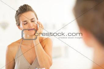Happy young woman applying cream in bathroom