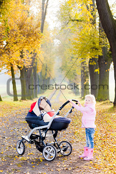 little girl with a pram on walk in autumnal alley