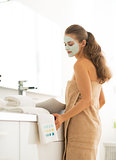 Young woman wearing facial cosmetic mask in bathroom