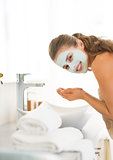 Young woman wearing facial cosmetic mask washing face