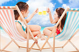 two sunshine girl holding beer cheers  on a beach chair