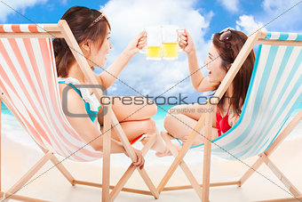 two sunshine girl holding beer cheers  on a beach chair
