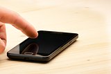 man's hand touching screen of black smartphone on wood desk