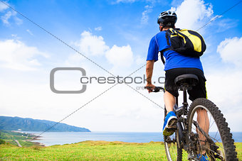 young man sitting on a  mountain bike and looking the ocean