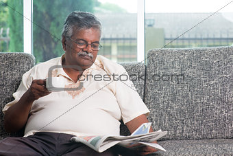 Indian senior adult drinking coffee while reading news paper 