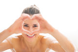Young woman in bathtub looking through heart shaped hands