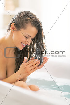 Young woman applying hair conditioner in bathtub
