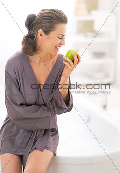 Happy young woman with apple near bathtub