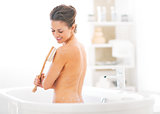 Young woman using body brush in bathtub