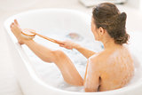 Young woman using body brush in bathtub. rear view