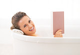 Happy young woman reading book in bathtub