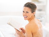 Portrait of happy young woman reading book in bathtub