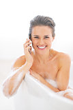 Happy young woman talking mobile phone in bathtub