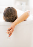 Young woman with cell phone laying in bathtub. rear view