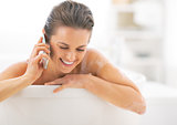 Happy young woman talking cell phone in bathtub