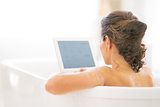 Young woman using tablet pc in bathtub. rear view