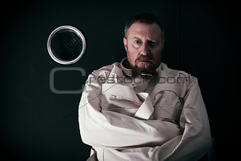 Insane man in a cell wearing a straitjacket