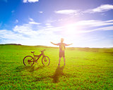 backpacker standing next to bicycle with sunrise background