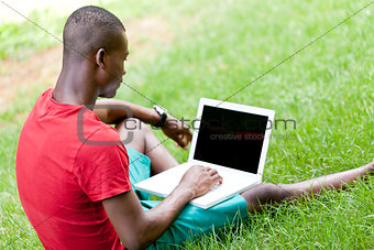young smiling african student sitting in grass with notebook