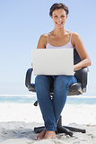 Pretty brunette using laptop on the beach sitting on swivel chair