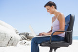 Pretty brunette using laptop on the beach sitting on swivel chair