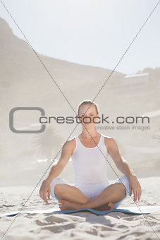 Smiling woman sitting in lotus pose on beach