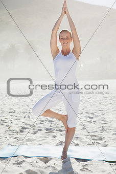 Smiling woman standing in tree pose on beach