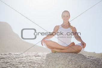 Smiling woman sitting in lotus pose on beach