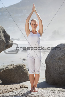 Blonde woman standing in tree pose on a rock