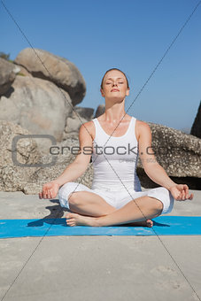 Blonde woman sitting in lotus pose on beach on mat
