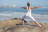 Blonde woman standing in warrior pose on beach on rock