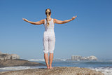 Blonde woman standing on beach on rock with arms out