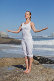 Blonde content woman standing on beach on rock with arms out