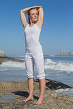 Blonde woman standing on rock stretching arms