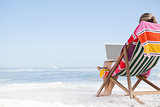 Woman sitting on beach in deck chair using laptop